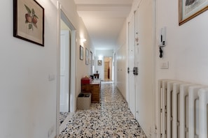 A hallway with a patterned floor, framed artwork on the walls, and a radiator on the right.