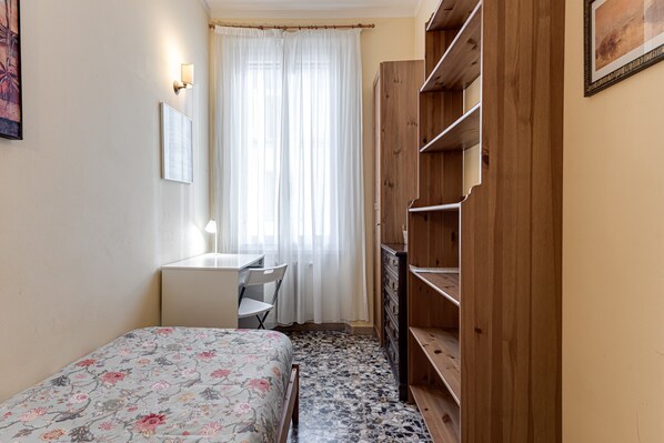 A bedroom with a bed, a desk, a chair, a wardrobe, and a window with curtains.