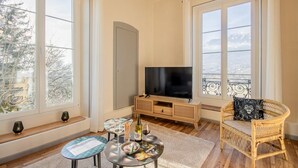 A living room with a TV, wicker furniture, and large windows offering a city view.