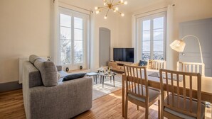 A modern living room with a sofa, dining table, chairs, a TV, and a chandelier.