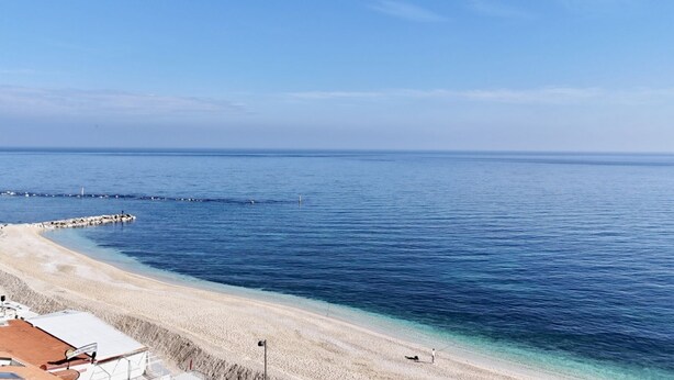A beach with clear blue water, a sandy shore, and a pier extending into the sea. - N276 - Numana, Spiaggiola beach front apartment (Numana)