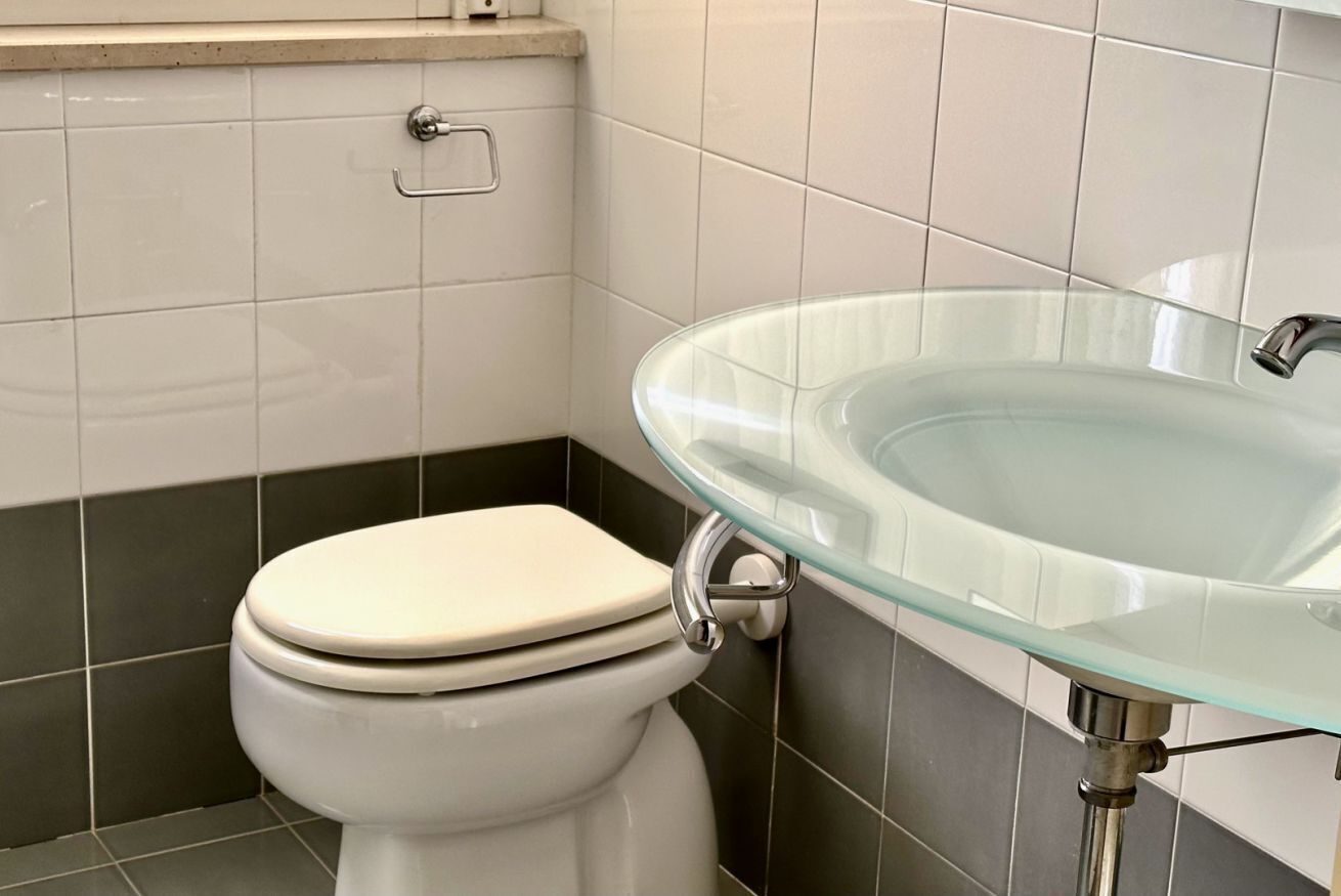Une salle de bain avec des toilettes, un lavabo en verre et des murs carrelés.
