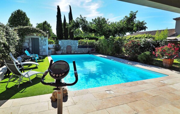 A swimming pool with a control panel in the foreground, surrounded by a garden with various plants and a stone wall. - Cozy home in Eyragues (Eyragues)