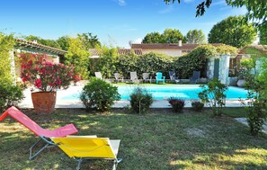 A backyard with a swimming pool, surrounded by greenery and a few lounge chairs. - Cozy home in Eyragues (Eyragues)