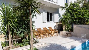 A poolside area with a seating arrangement, a small table, and a variety of plants.