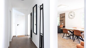 A hallway with a door, a wall-mounted mirror, and a dining area with a table and chairs.