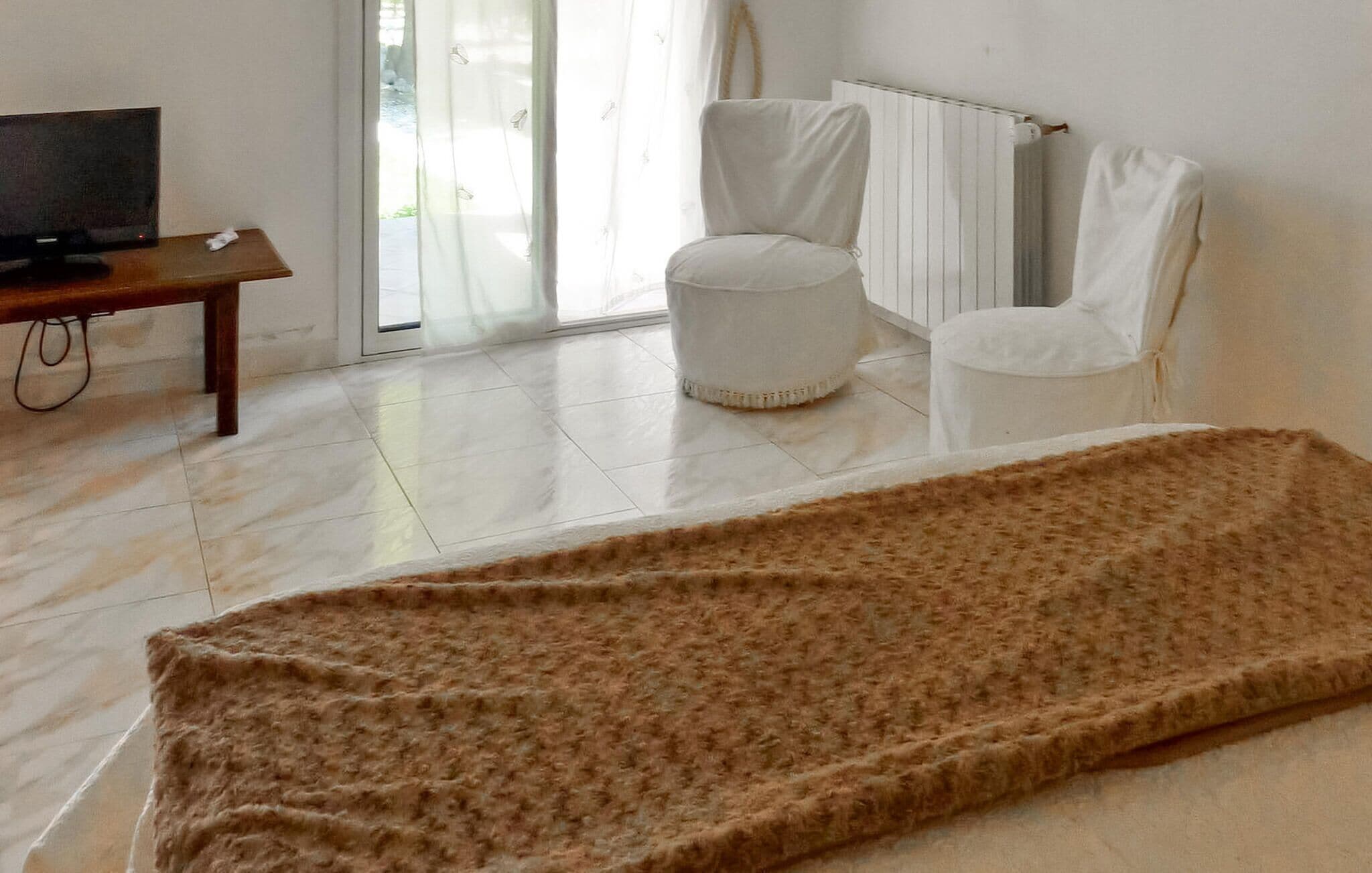 A room with a bed, a television on a wooden table, a white chair, and a radiator.