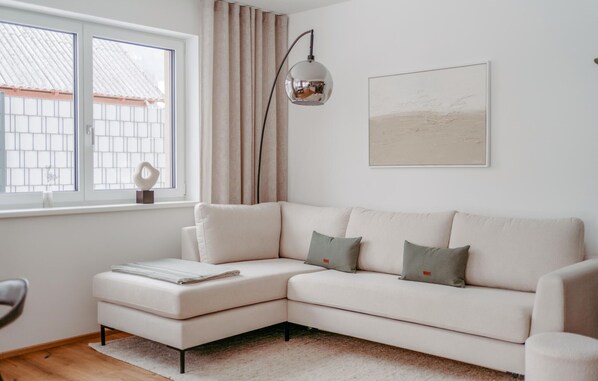 Un salon moderne avec un canapé d’angle, une lampe sur pied et une fenêtre avec des rideaux.