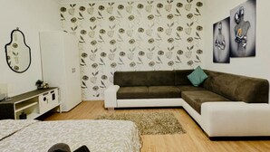 Un dormitorio moderno con un sofá marrón, una mesita de noche blanca, una cama con ropa de cama estampada y papel tapiz floral.