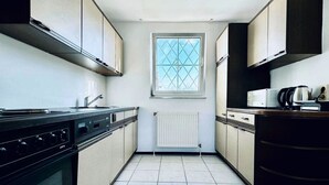 Una cocina con estufa, microondas y hervidor, una ventana con diseño de cuadrícula y un radiador.