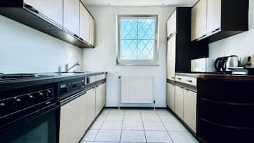 A kitchen with a stove, microwave, and kettle, a window with a grid pattern, and a radiator.