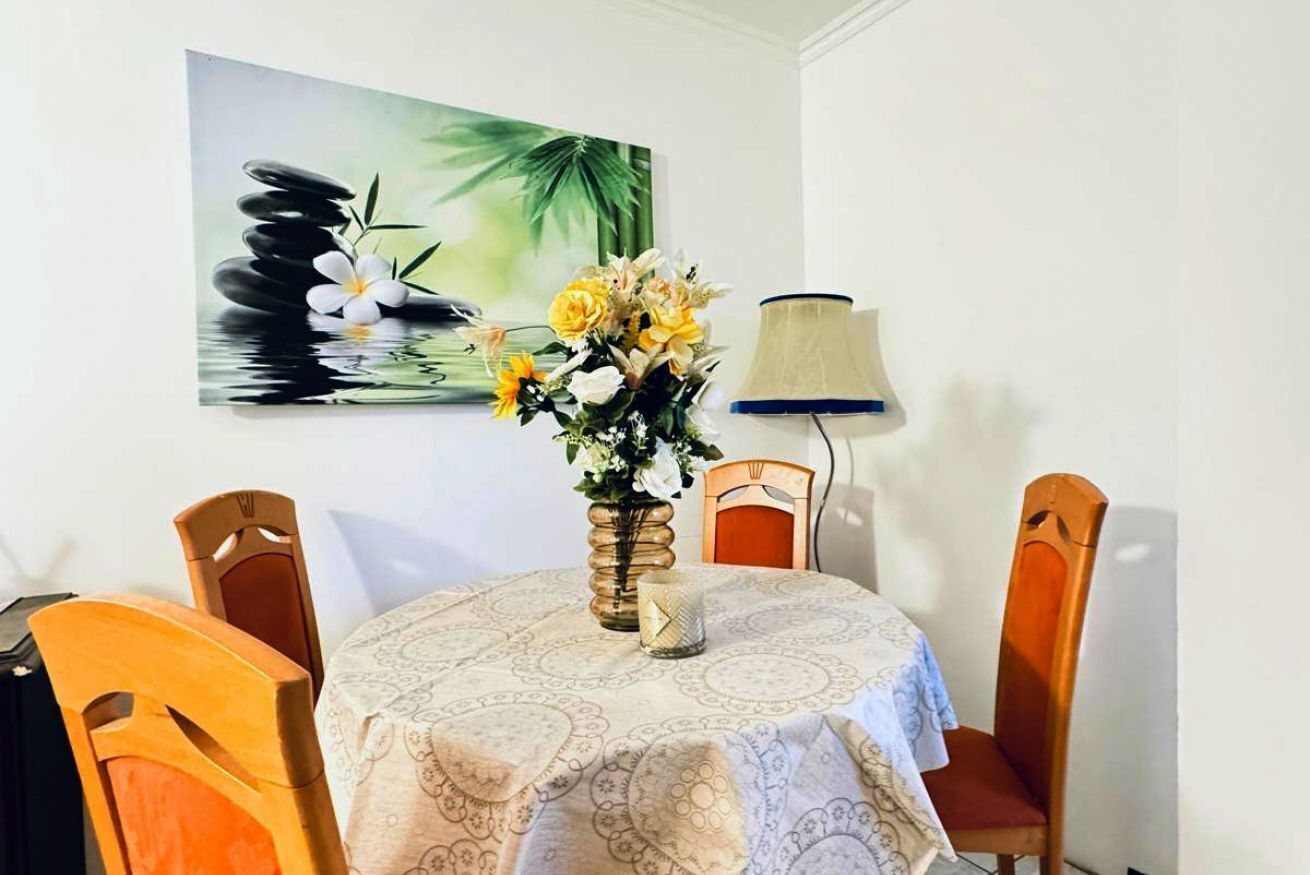 A dining table with a patterned tablecloth, a vase with flowers, and a painting on the wall.