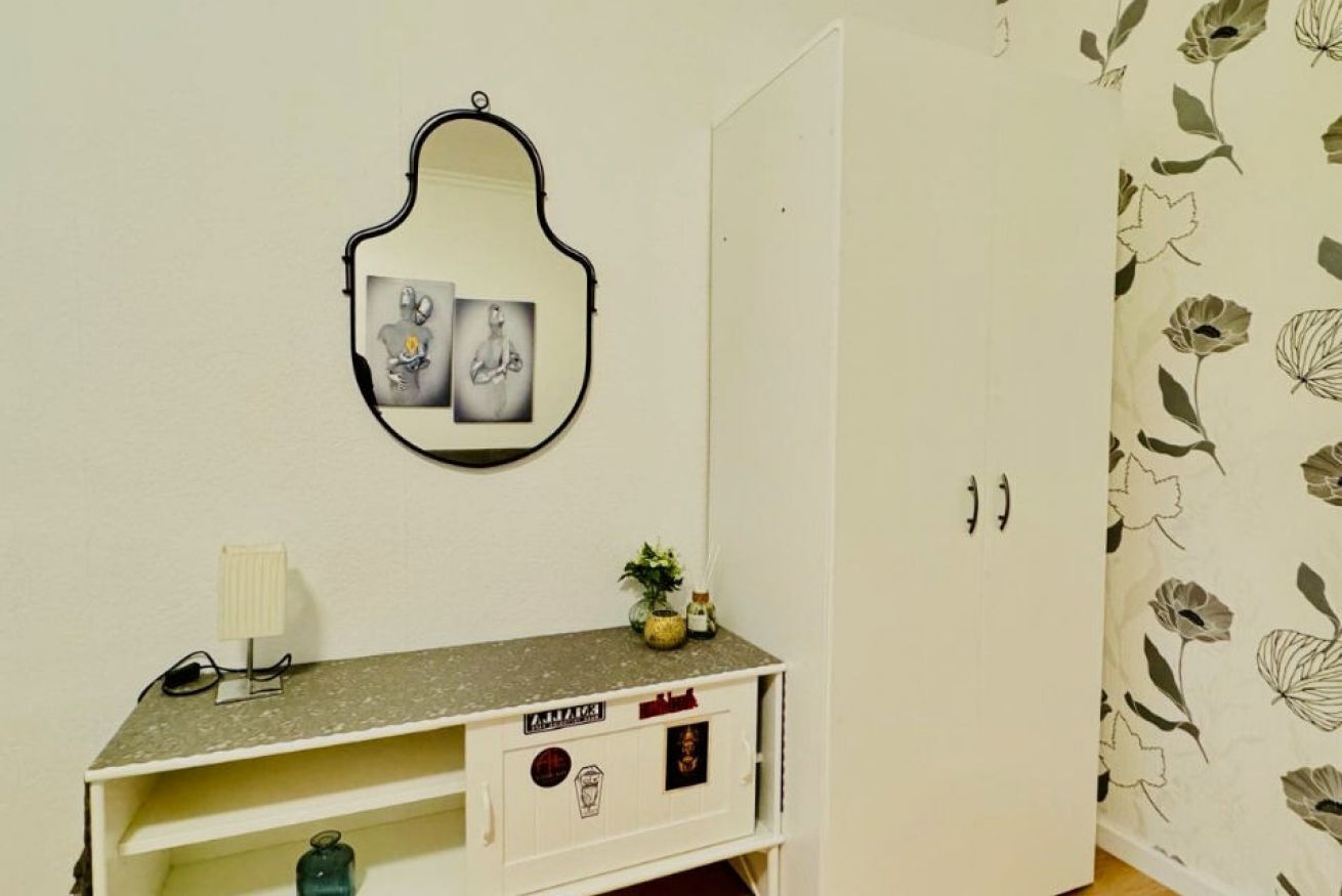 A room with a mirror, a small cabinet with a floral pattern, and a wall with a floral wallpaper design.