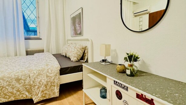 Un dormitorio con cama, cómoda, espejo, ventana con cortinas y radiador.