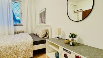 A bedroom with a bed, a dresser, a mirror, a window with curtains, and a radiator.