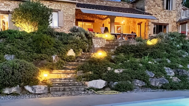 Un edificio de piedra con piscina, escalones que conducen a una zona cubierta e iluminación exterior.