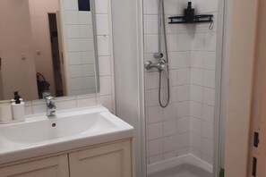 Casa de banho com lavatório branco, espelho e chuveiro.