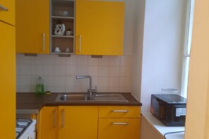 Cucina con pensili gialli, lavello in acciaio inossidabile, forno a microonde e piano cottura a gas.