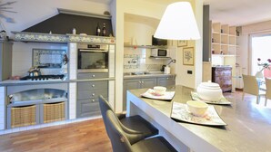 A modern kitchen with a gas stove, oven, microwave, and a dining area with a bar stool and a table set with a teapot and cups. - Awesome home in Bergamo with WiFi (Bergamo)