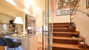 A modern kitchen with a central island, bar stools, and a staircase leading to a loft area with bookshelves and artwork. - Awesome home in Bergamo with WiFi (Bergamo)