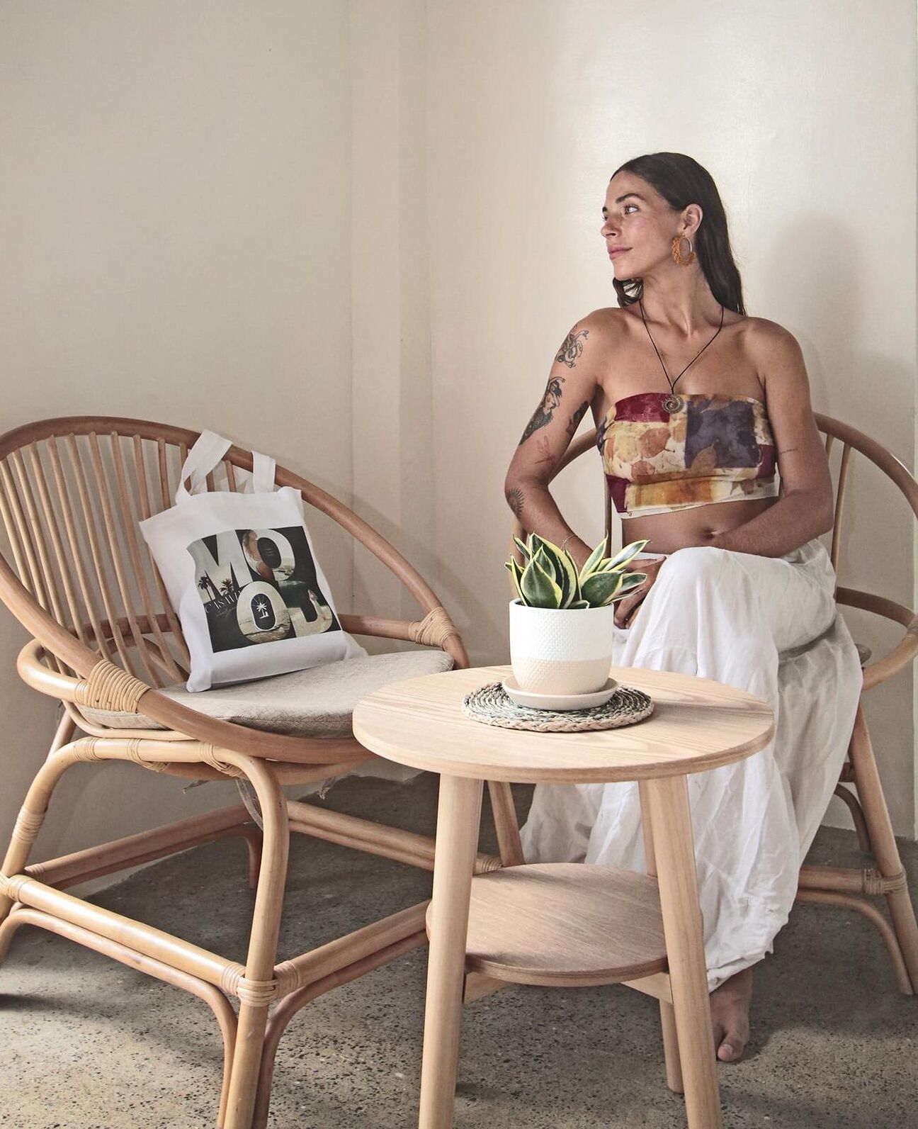 A person sitting on a wicker chair with a small round table in front, holding a potted plant.