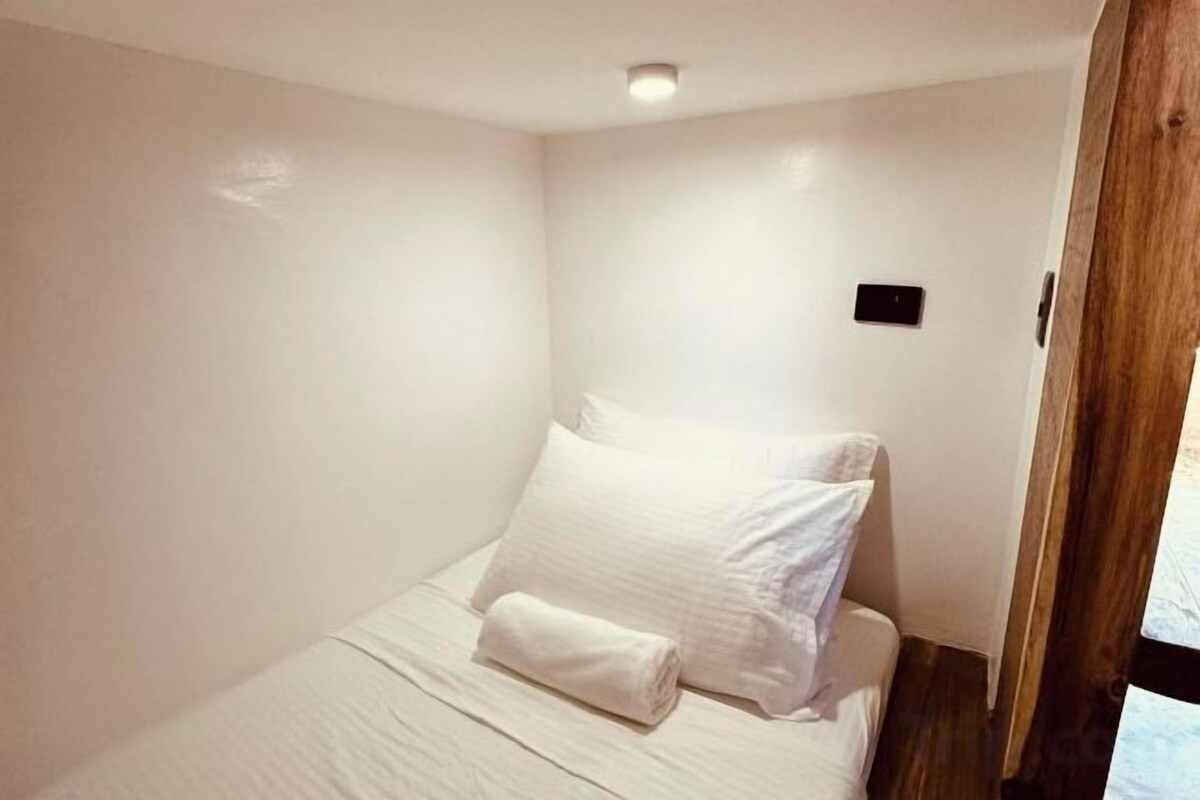 A single bed with a white duvet and pillows, a wooden headboard, and a small wall-mounted light fixture.