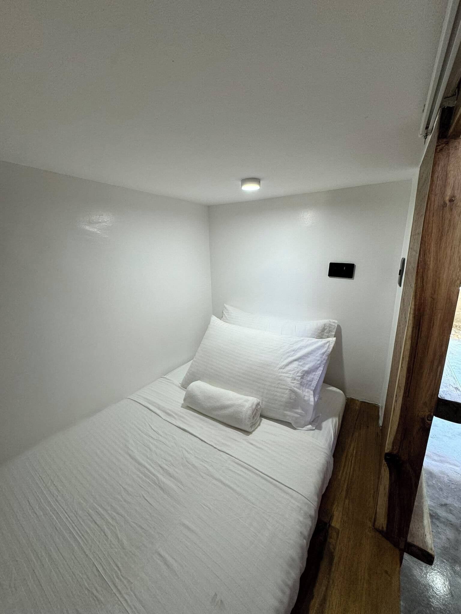 A small, white, single-bed room with a wooden floor and a small window.