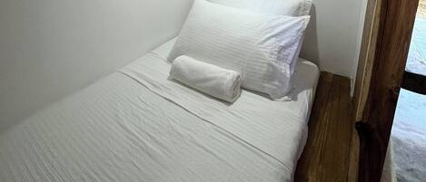 A small, white, single-bed room with a wooden floor and a small window.