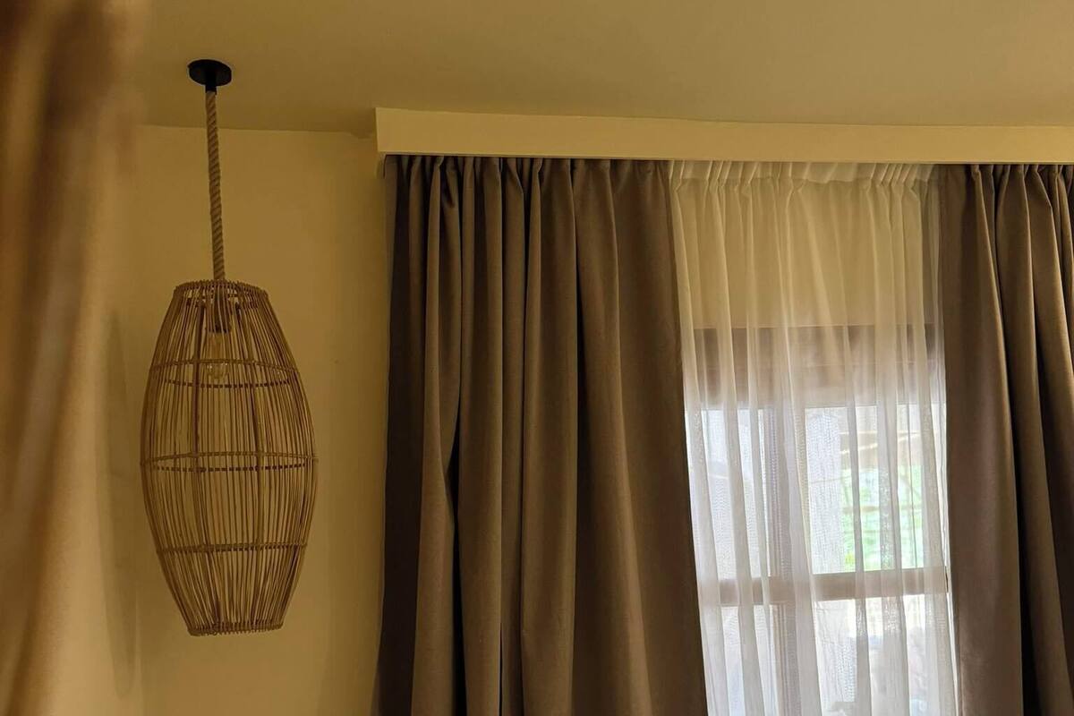 A bedroom with a bed, a hanging light fixture, and a window with curtains.