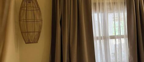 A bedroom with a bed, a hanging light fixture, and a window with curtains.