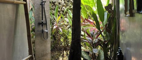 Un bagno con zona doccia, una scala in legno, un muro in pietra e diverse piante.