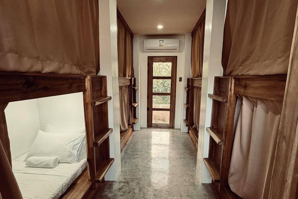 A corridor with bunk beds on either side, a central door, and an air conditioning unit above it.