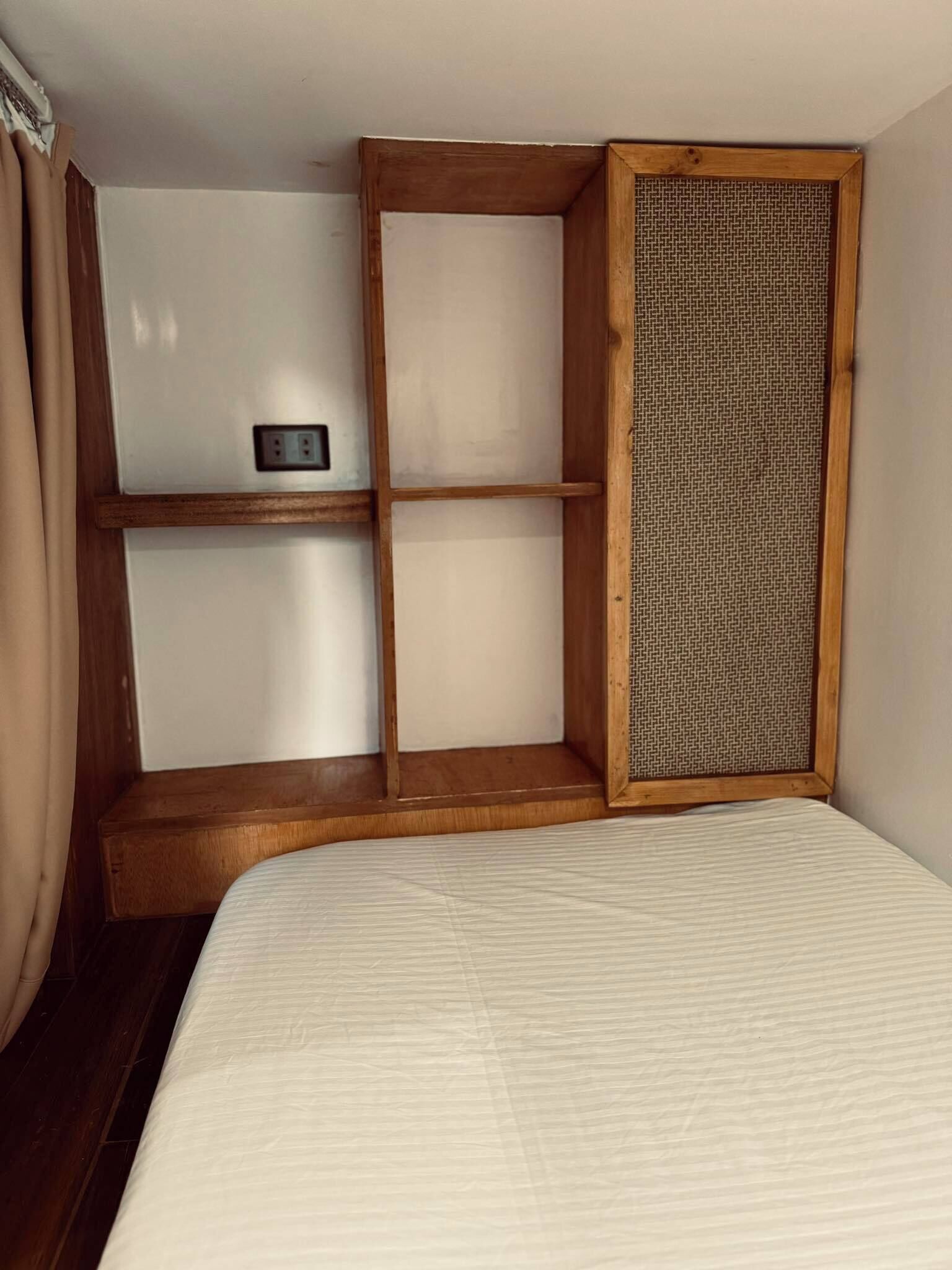 A bedroom with a bed, a shelf unit, and a window with a woven blind.