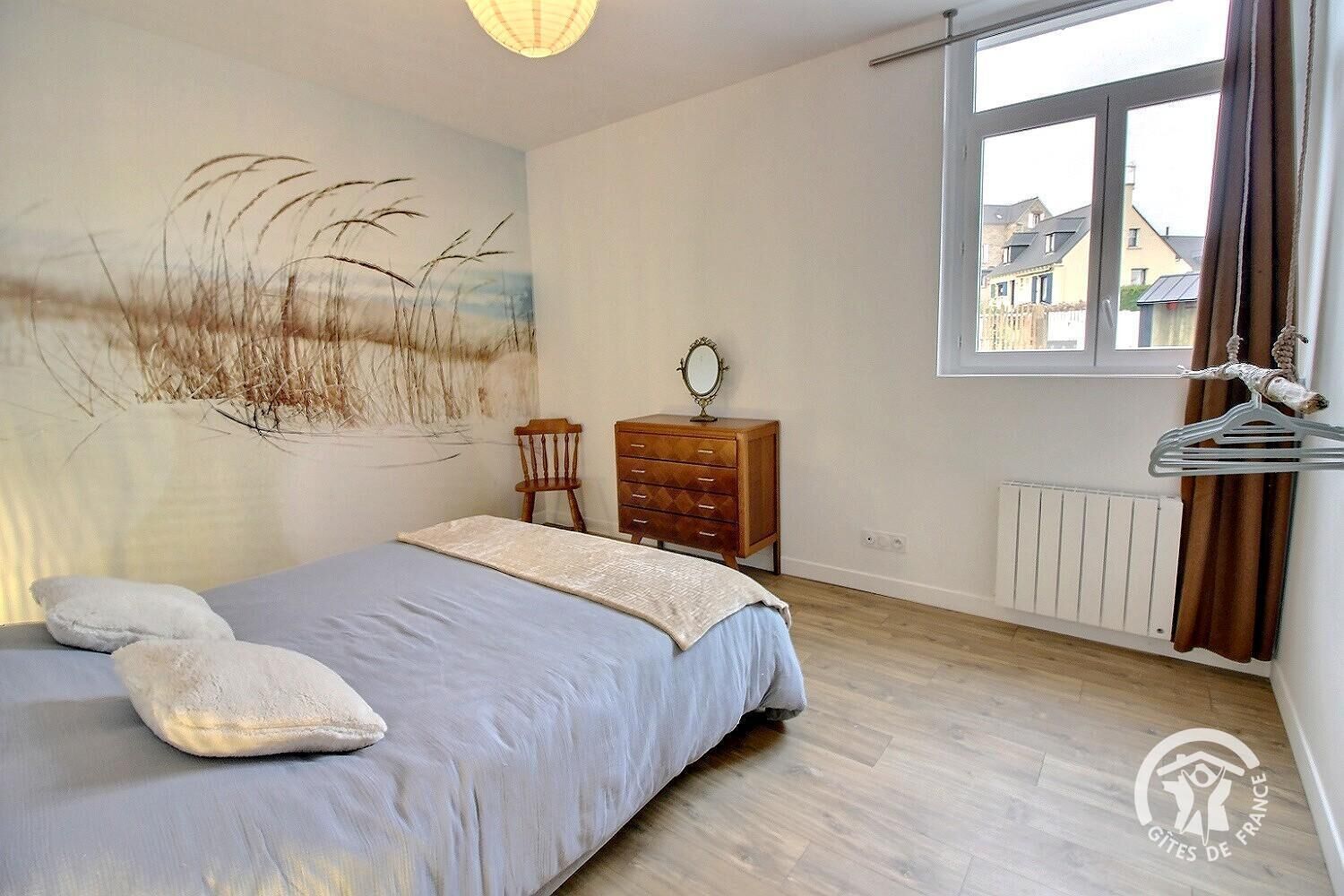 Une chambre à coucher avec un lit, une commode et une fenêtre donnant sur des maisons.