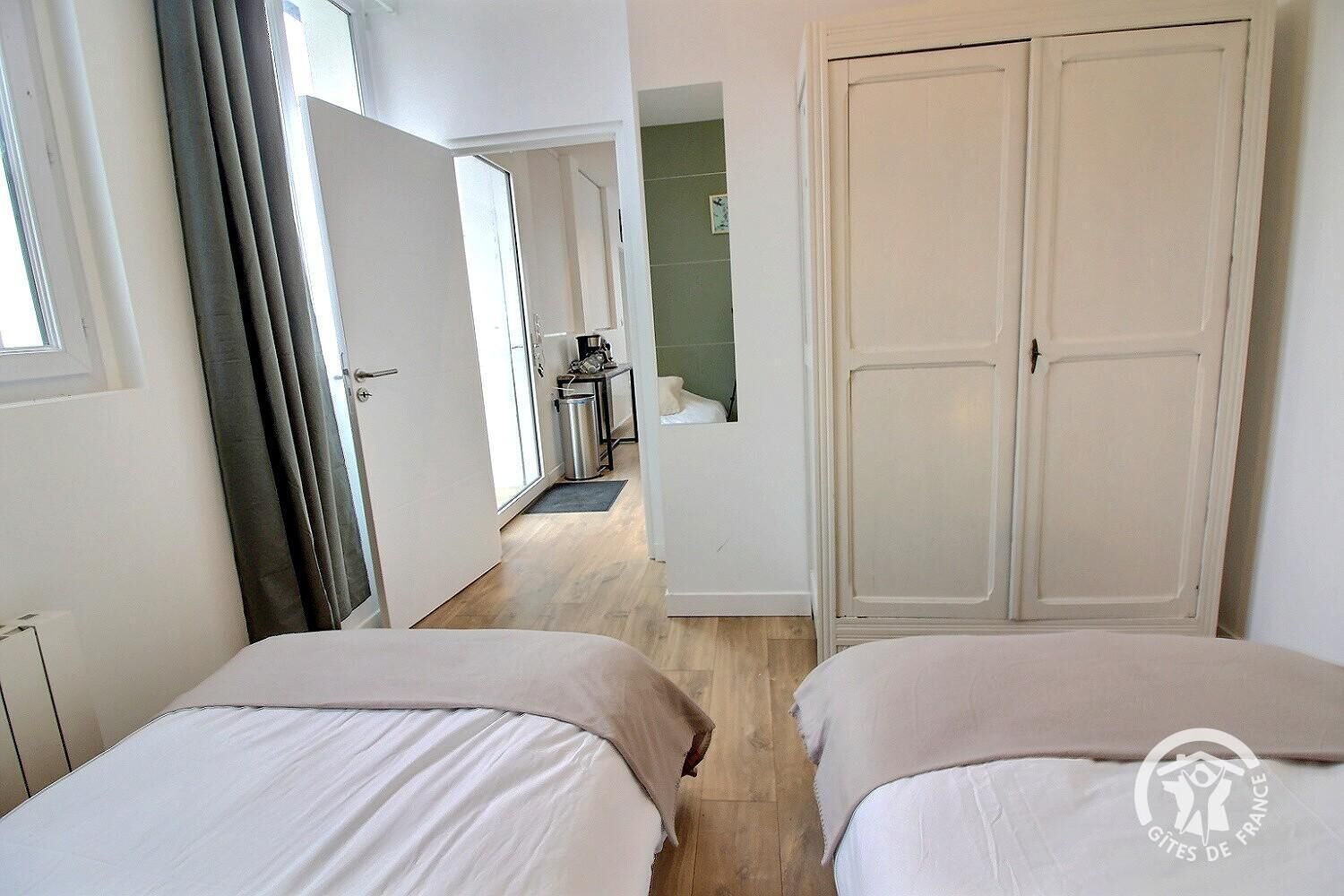 Een hotelkamer met twee bedden, een grote kledingkast en uitzicht op de gang.