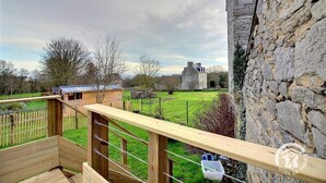 A wooden deck with a view of a stone wall, a grassy field, and a stone building in the distance. - Pen-guen - Saint Cast LE Guildo (SAINT CAST LE GUILDO)
