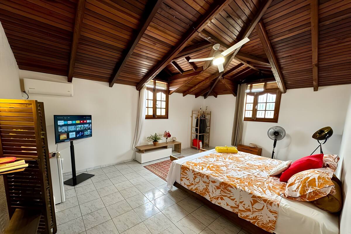A bedroom with a bed, a TV, a ceiling fan, and a window.