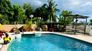 A swimming pool with clear water, surrounded by potted plants and a wooden deck. - Le Domaine du Val de l'Orge (Vieux-Habitants)