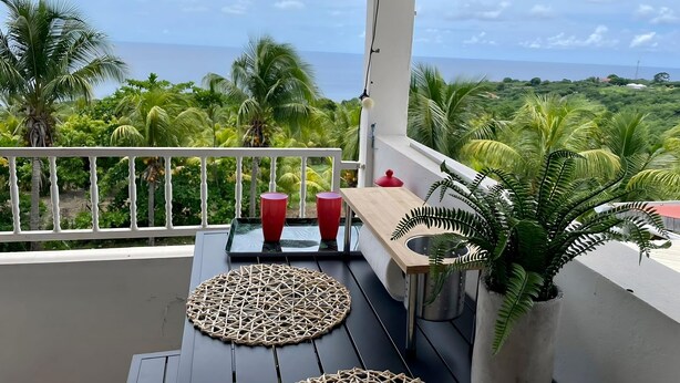 A balcony with a view of the sea, two red cups, and a woven mat. - Le Domaine du Val de l'Orge (Vieux-Habitants)