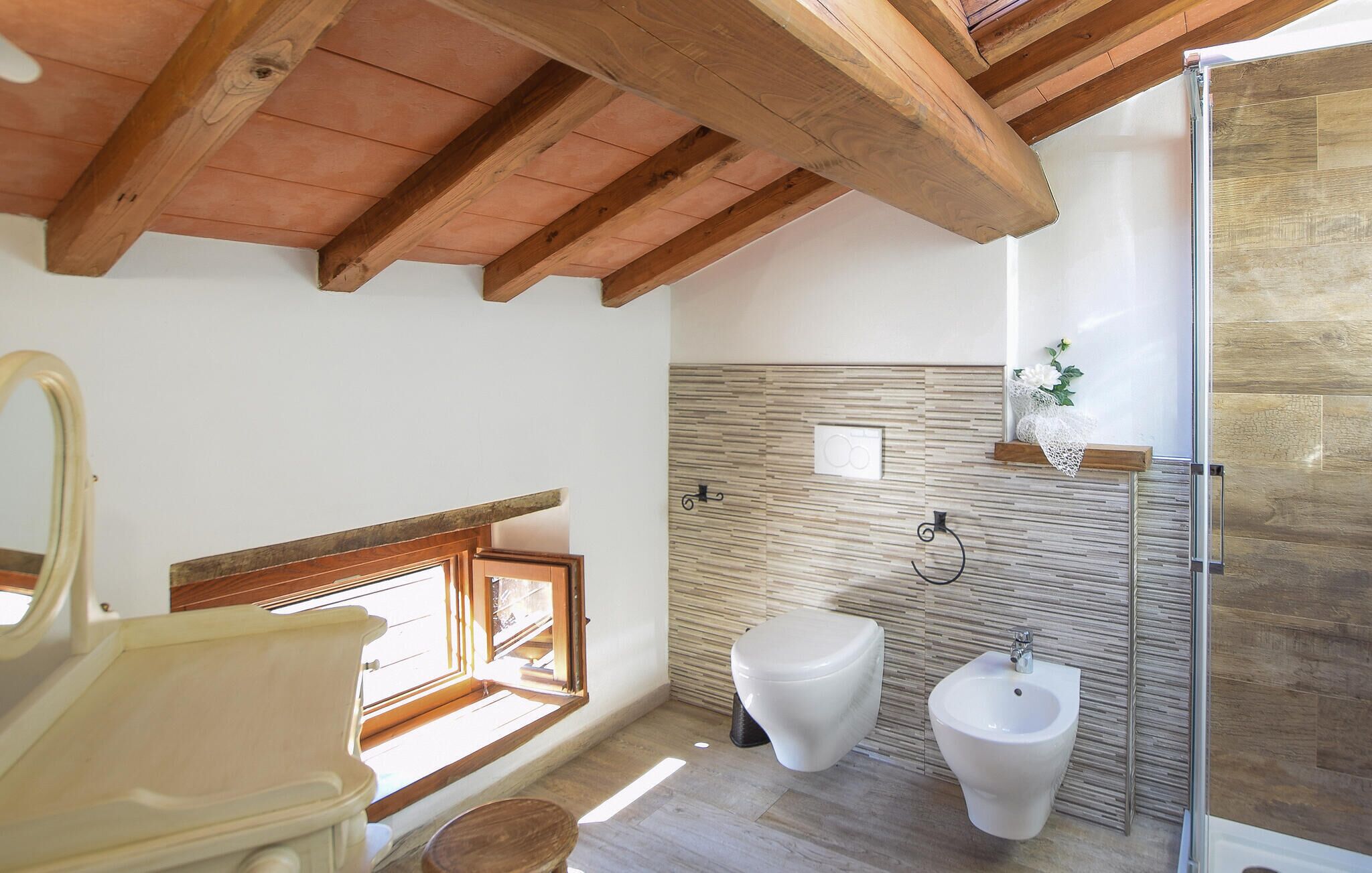 Een badkamer met een houten plafond, een bidet, een toilet en een raam met uitzicht.