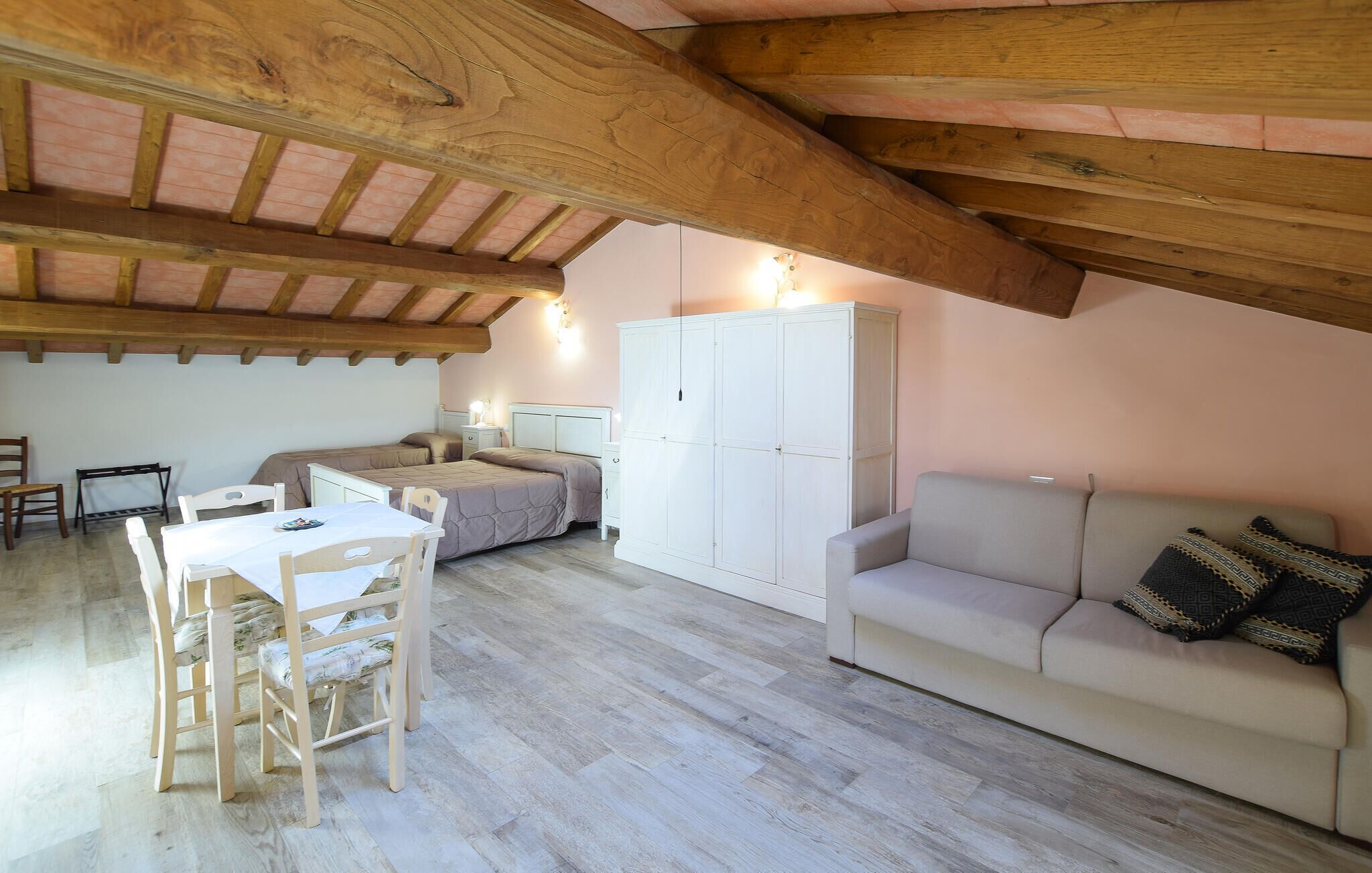 Une chambre confortable située sous les combles, avec un plafond en bois, une grande armoire, un canapé et une table à manger avec des chaises.