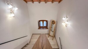 Una escalera con escalones de madera y una viga de techo de madera, flanqueada por apliques de pared y un espejo.