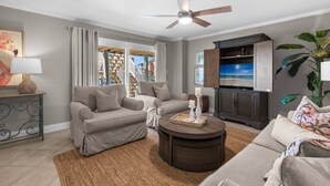 A living room with a sofa, a coffee table, a TV, and a ceiling fan. - Boardwalk A4 | Pool, Beach Access | New Renovations! (Pensacola Beach)