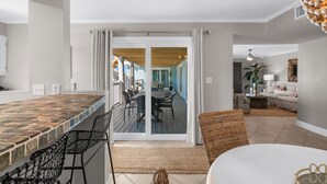 A modern kitchen with a tiled backsplash, a dining area with a wooden table and chairs, and a living room with a sofa and a coffee table. - Boardwalk A4 | Pool, Beach Access | New Renovations! (Pensacola Beach)