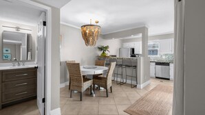 A modern kitchen with white cabinets, a dining area with wicker chairs, and a central chandelier. - Boardwalk A4 | Pool, Beach Access | New Renovations! (Pensacola Beach)