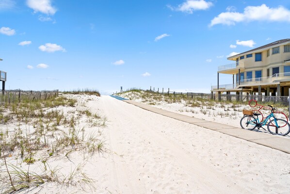 A beachside pathway with a bicycle, a sandy beach, and a building with multiple balconies.