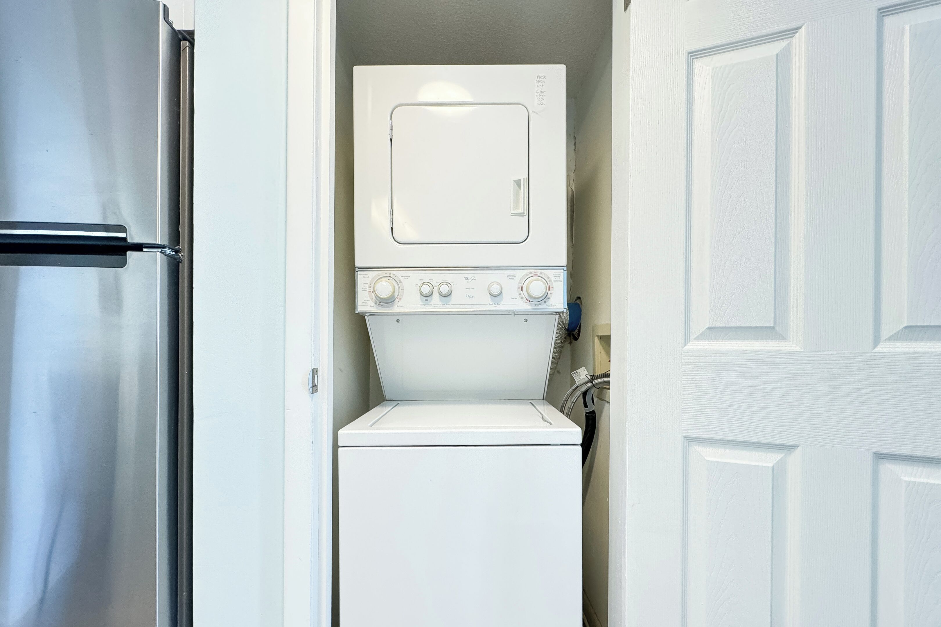 Une petite buanderie équipée d’un lave-linge et d’un sèche-linge à chargement frontal, d’un réfrigérateur en acier inoxydable et d’une porte blanche.