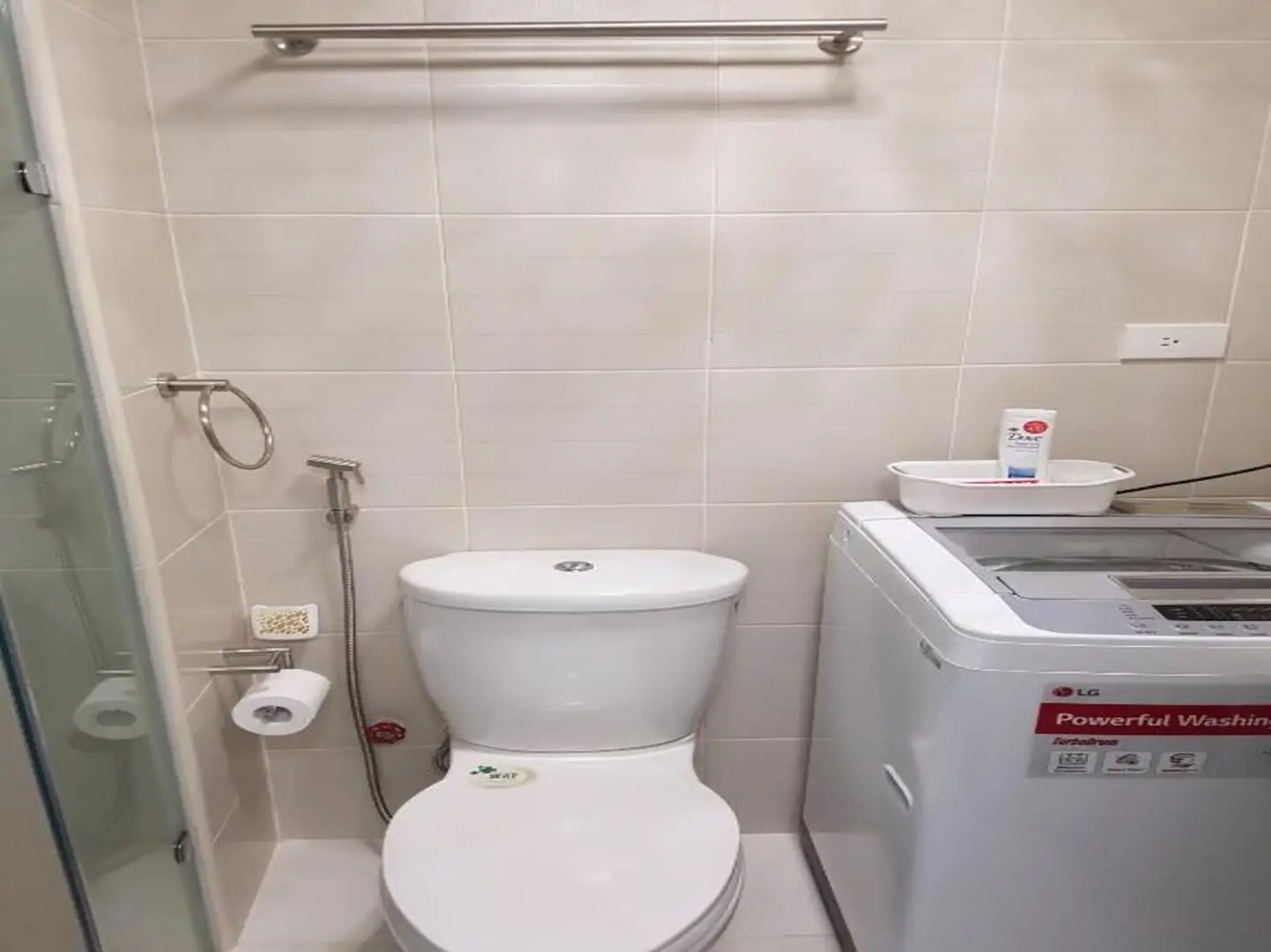Un baño con inodoro, cabina de ducha de vidrio y lavadora.