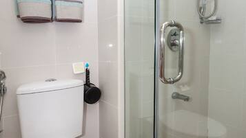 A bathroom with a toilet, a glass shower enclosure, and a towel rack with striped towels.