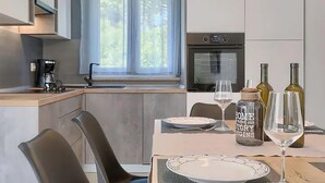 A modern kitchen with a window, a coffee maker, and a dining area with wine glasses and bottles. - Stunning home in Labin (Labin)